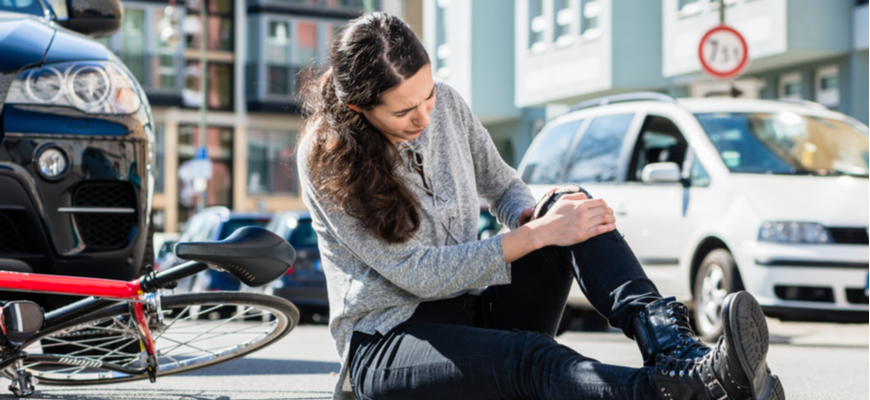 car accident pain and suffering woman holding her knee sitting by car accident