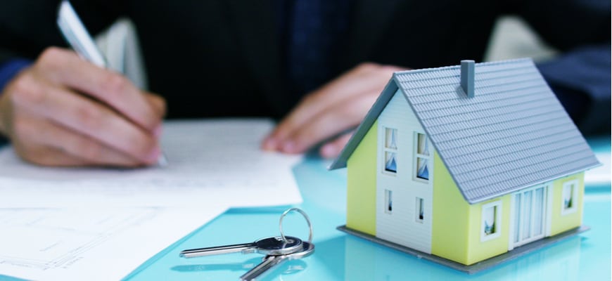 A real estate lawyer signs paper with housekeys in the foreground.